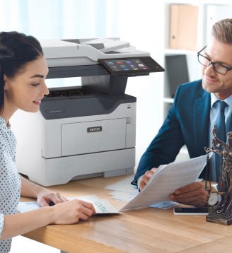 Ein Mann und eine Frau sitzen an einem Tisch und unterhalten sich, während in der Nähe ein Xerox®-Drucker steht.